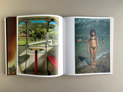 Open Index — Christopher Anderson booklet with a window view and a child standing in shallow water by a mountain lake.