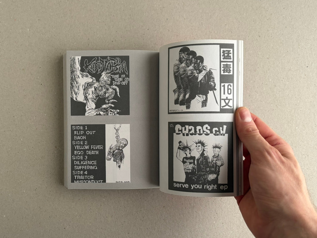 Open book showing black-and-white punk graphics and Japanese text, held at the right edge by a hand.