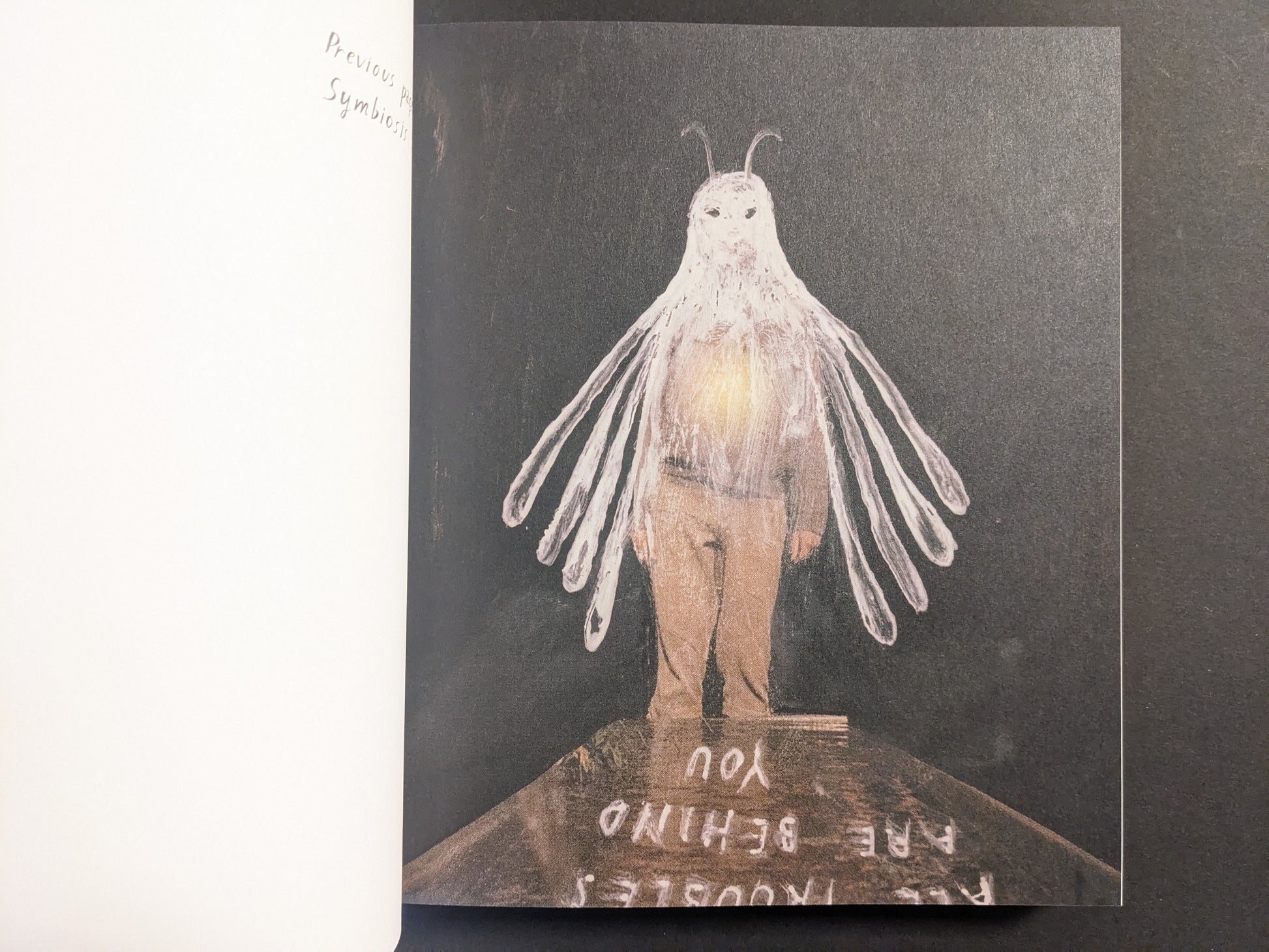Interior artwork from “In a Dark Time, the Eye Begins to See” by Julia Soboleva, showing a moth-like figure with long, wing-like arms on a dark background.