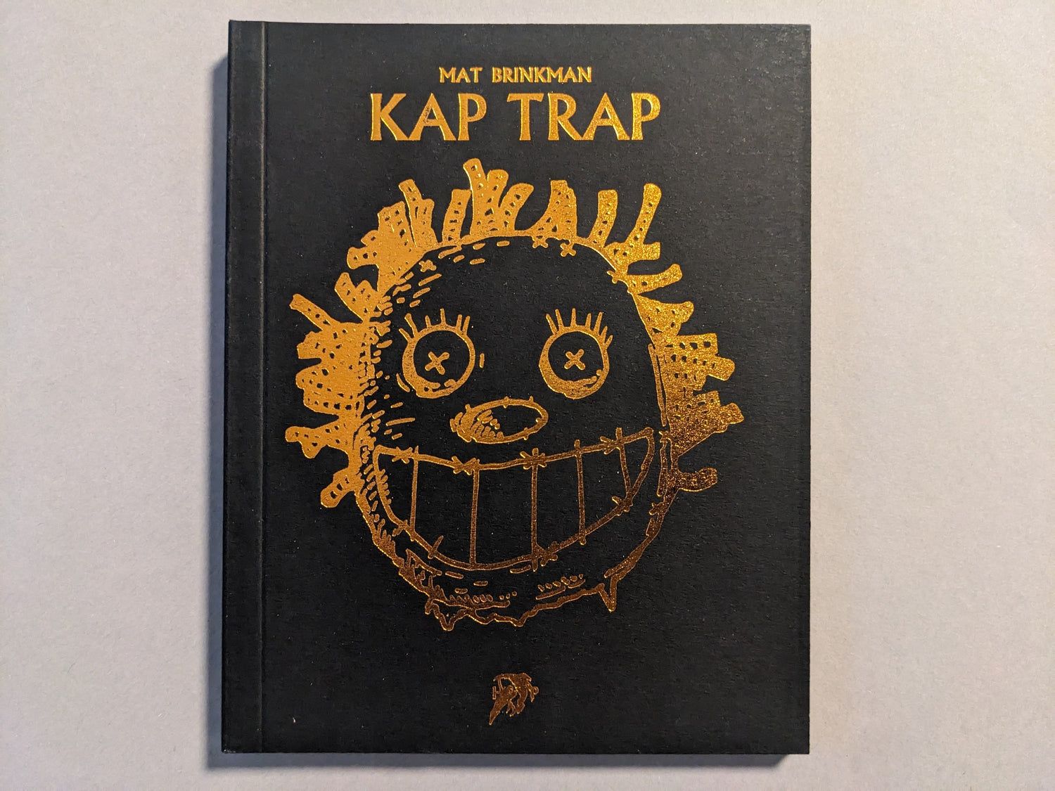 Front cover of KAP TRAP by Mat Brinkman, black hardcover with gold foil illustration.