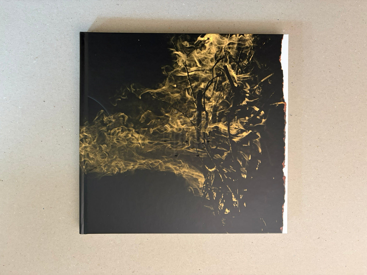 Kurayami closed and seen from above, with the black cover and gold smoke-like image centered on a grey surface.