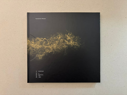 Kurayami by Masao Yamamoto, front cover on a beige surface, with a black cover and a gold smoke-like image across the centre.