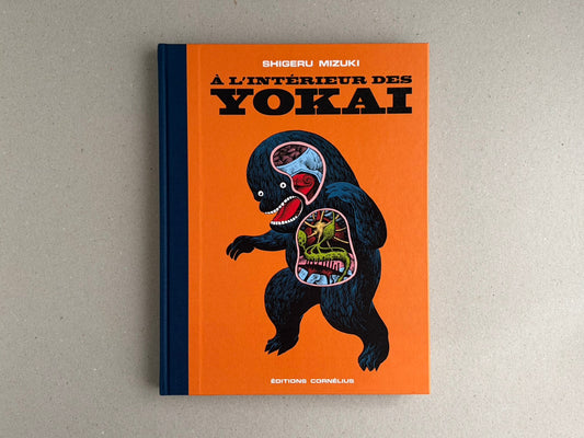 Front cover of À l'interieur des yokai by Shigeru Mizuki, orange hardcover with a dark blue spine and a black yokai figure on the cover.