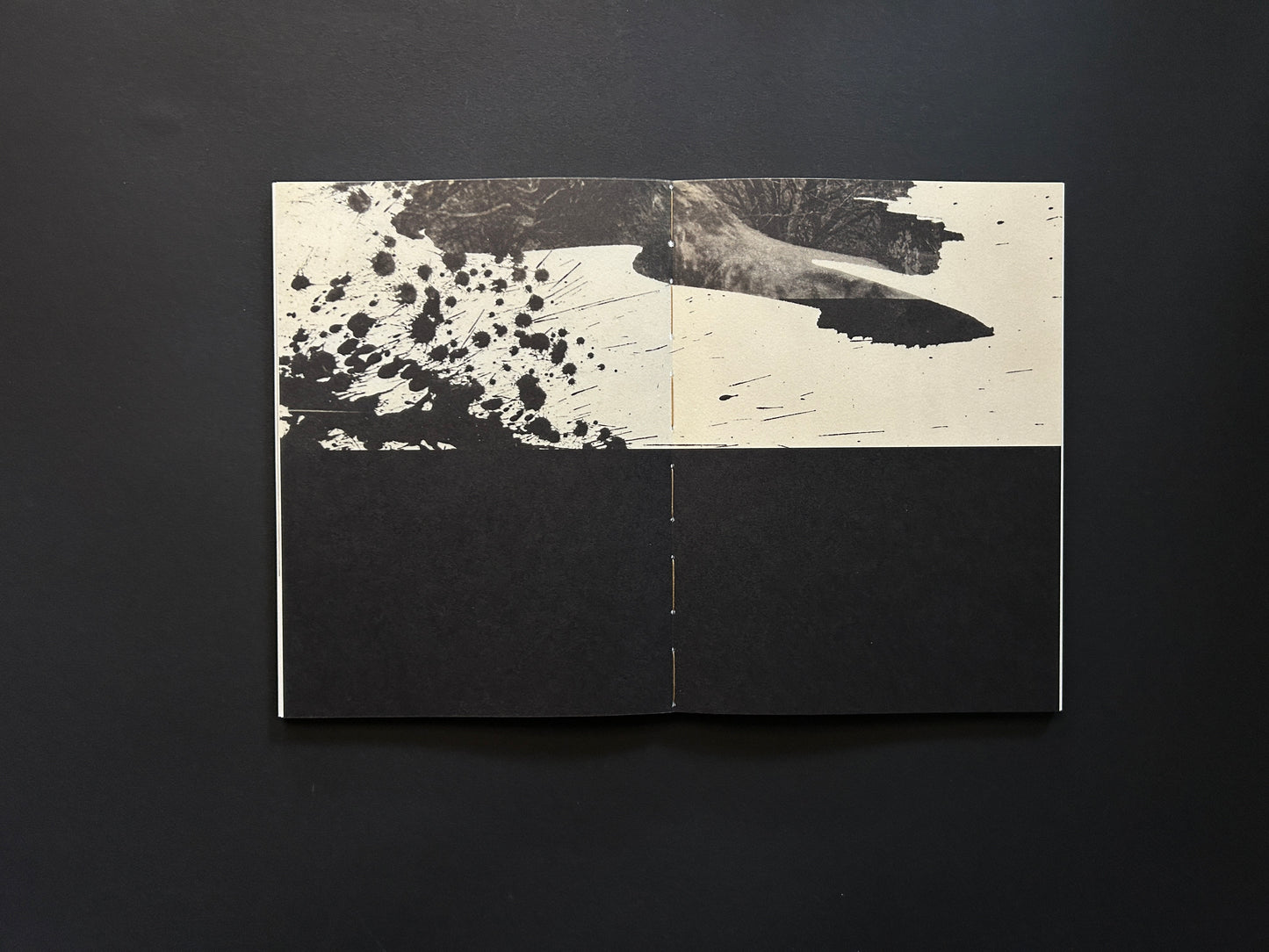 Open spread from Lejos De La Tierra with black ink splatter across the top and a visible stitched binding at the centre
