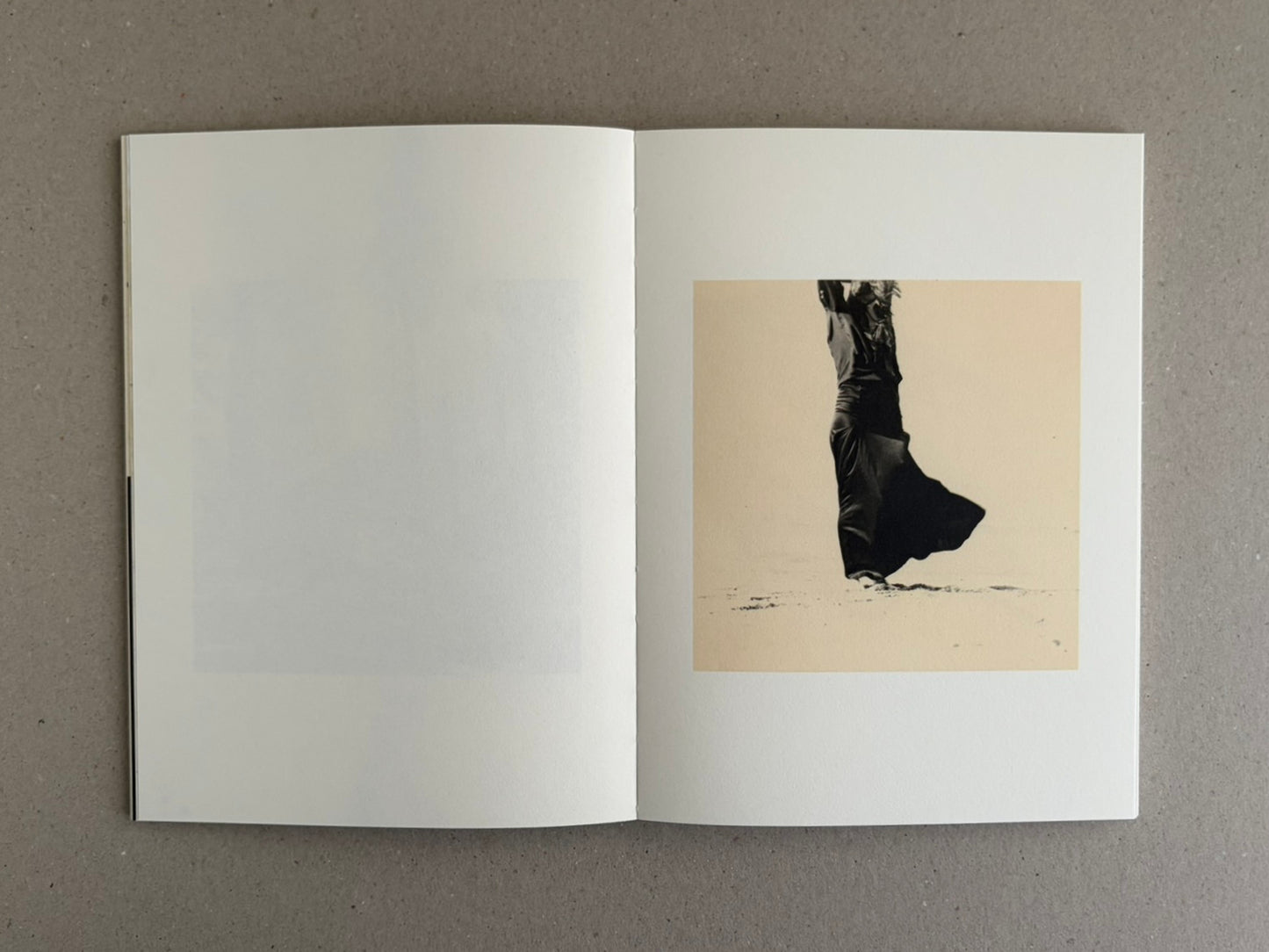 Open photobook spread from Lejos De La Tierra – Irene Zottola, showing a mostly blank left page and a small square image on the right page of a dark-clad figure against a pale background.