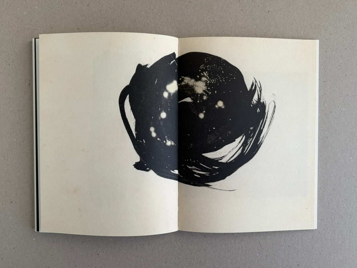 Open photobook spread from Lejos De La Tierra by Irene Zottola, showing a large black circular ink image across the center fold on off-white pages.