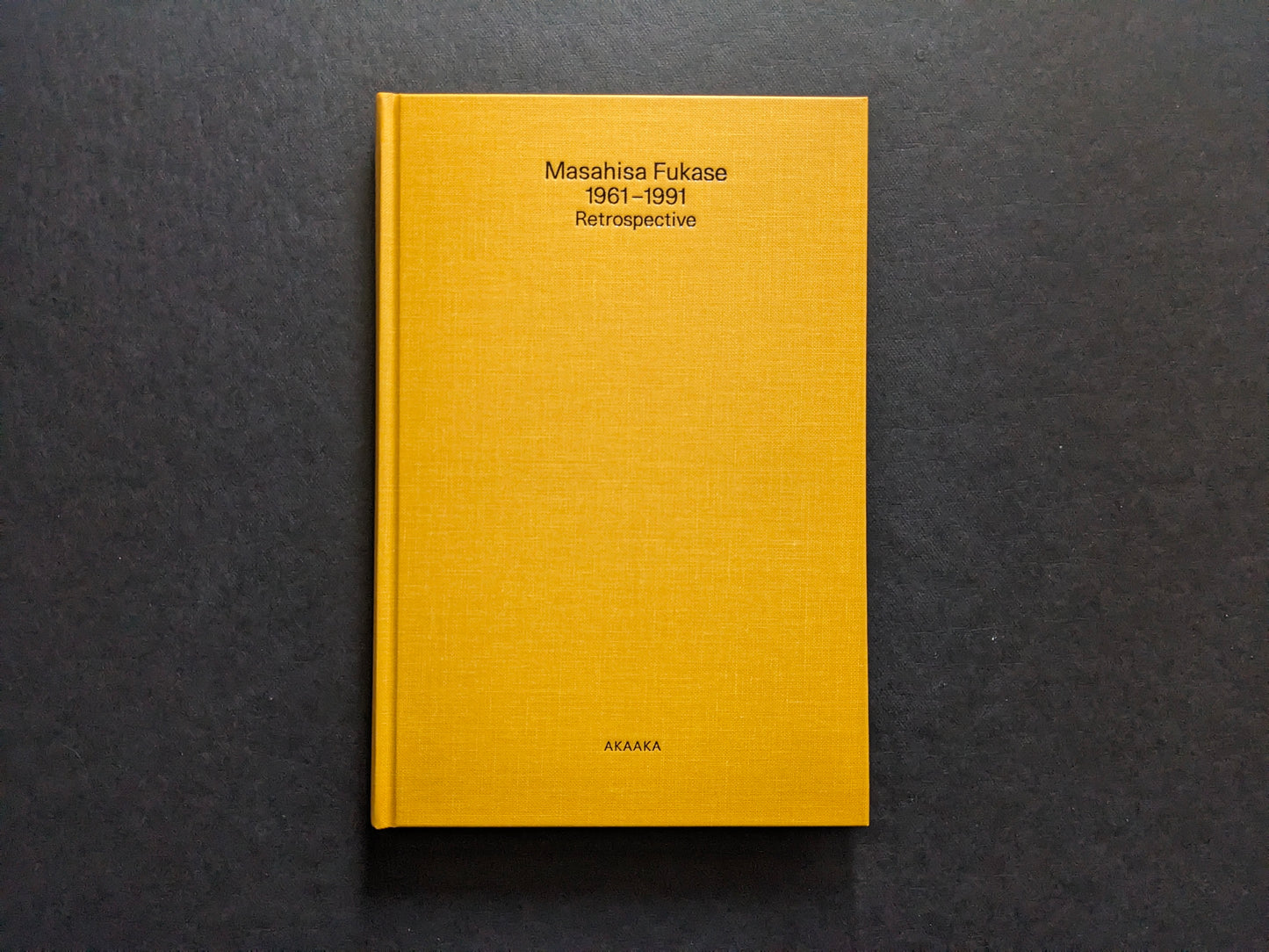 Front cover of Masahisa Fukase 1961–1991 Retrospective, yellow cloth hardcover with black title and AKAAKA imprint.