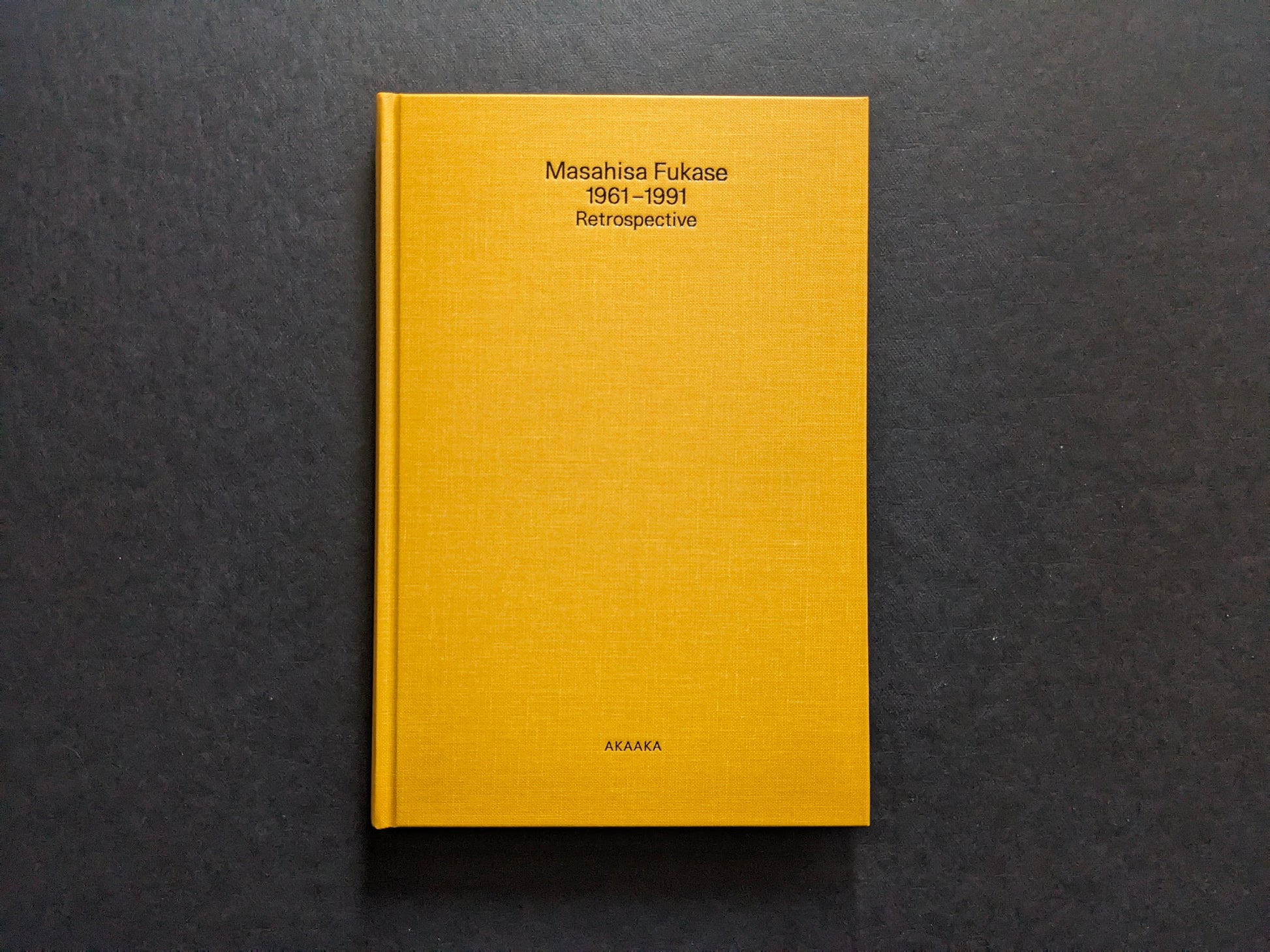 Front cover of Masahisa Fukase 1961–1991 Retrospective, yellow cloth hardcover with black title and AKAAKA imprint.