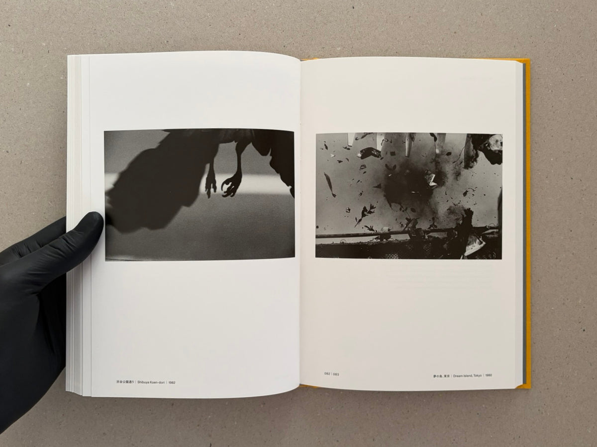Open spread from Masahisa Fukase 1961–1991 Retrospective showing two black-and-white photographs with page numbers 082 and 083, held open by a gloved hand.