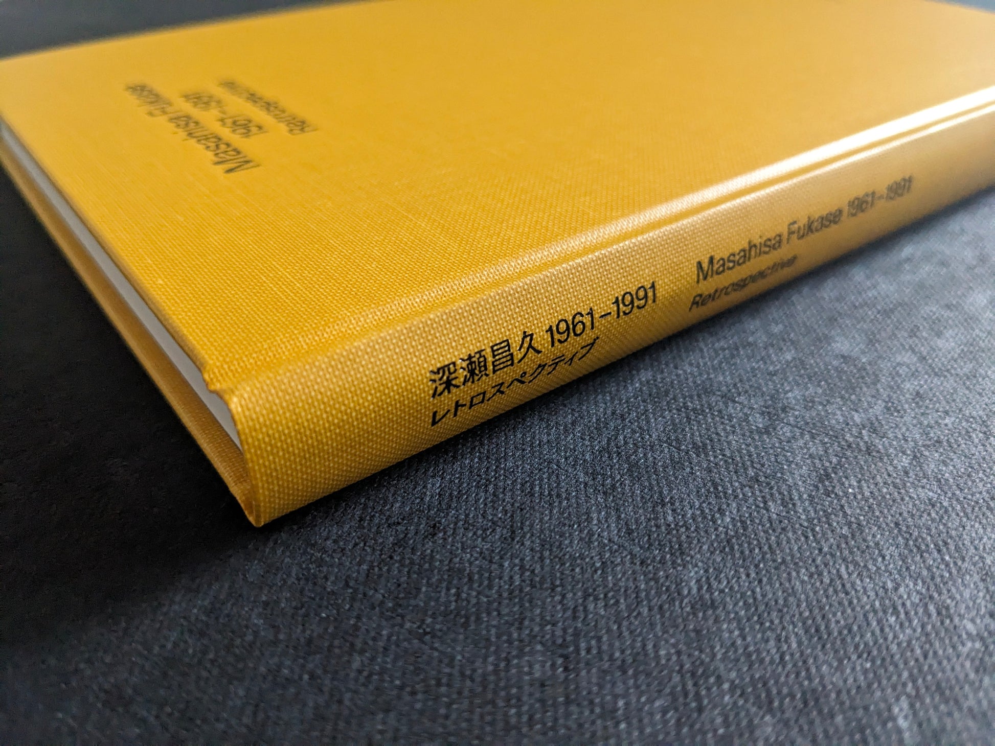 Spine detail of “Masahisa Fukase 1961–1991 Retrospective” showing Japanese and English title on yellow cloth.