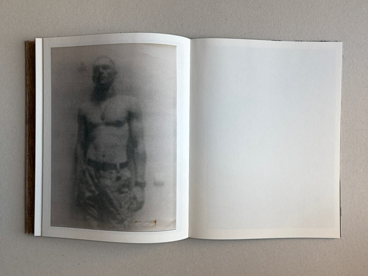 Materia by Vic Bakin, open photobook spread with a faded monochrome portrait on the left page and a blank right page.