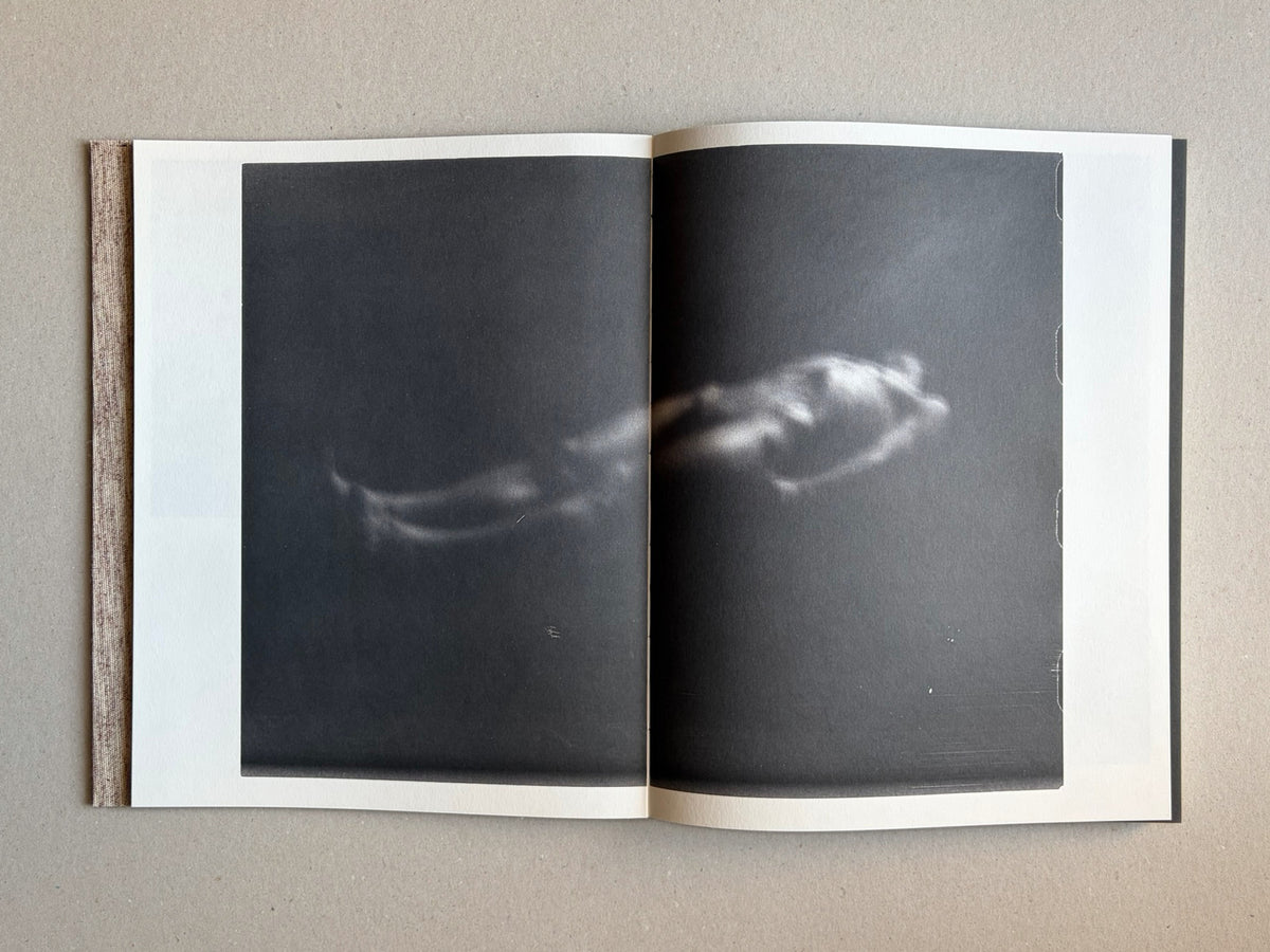 Open spread from Materia by Vic Bakin, showing a dark, blurred photographic image across two pages with a cloth spine visible at left.