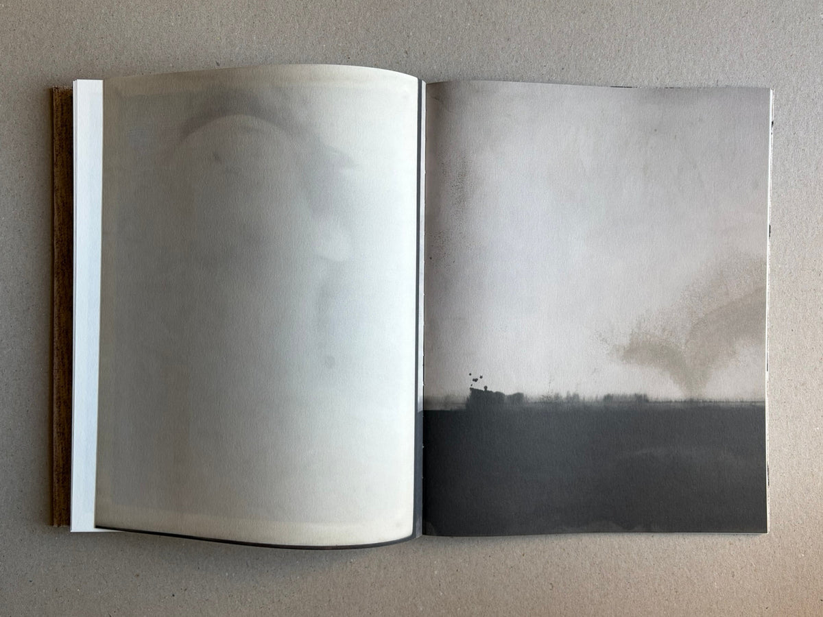 Open spread of Materia by Vic Bakin, showing a pale, faded image across the left page and a darker abstract image on the right page.
