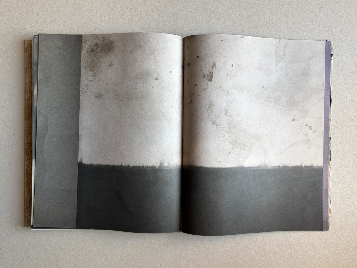 Open spread from Materia by Vic Bakin, showing a faded monochrome image with stains and a dark band across the lower half.