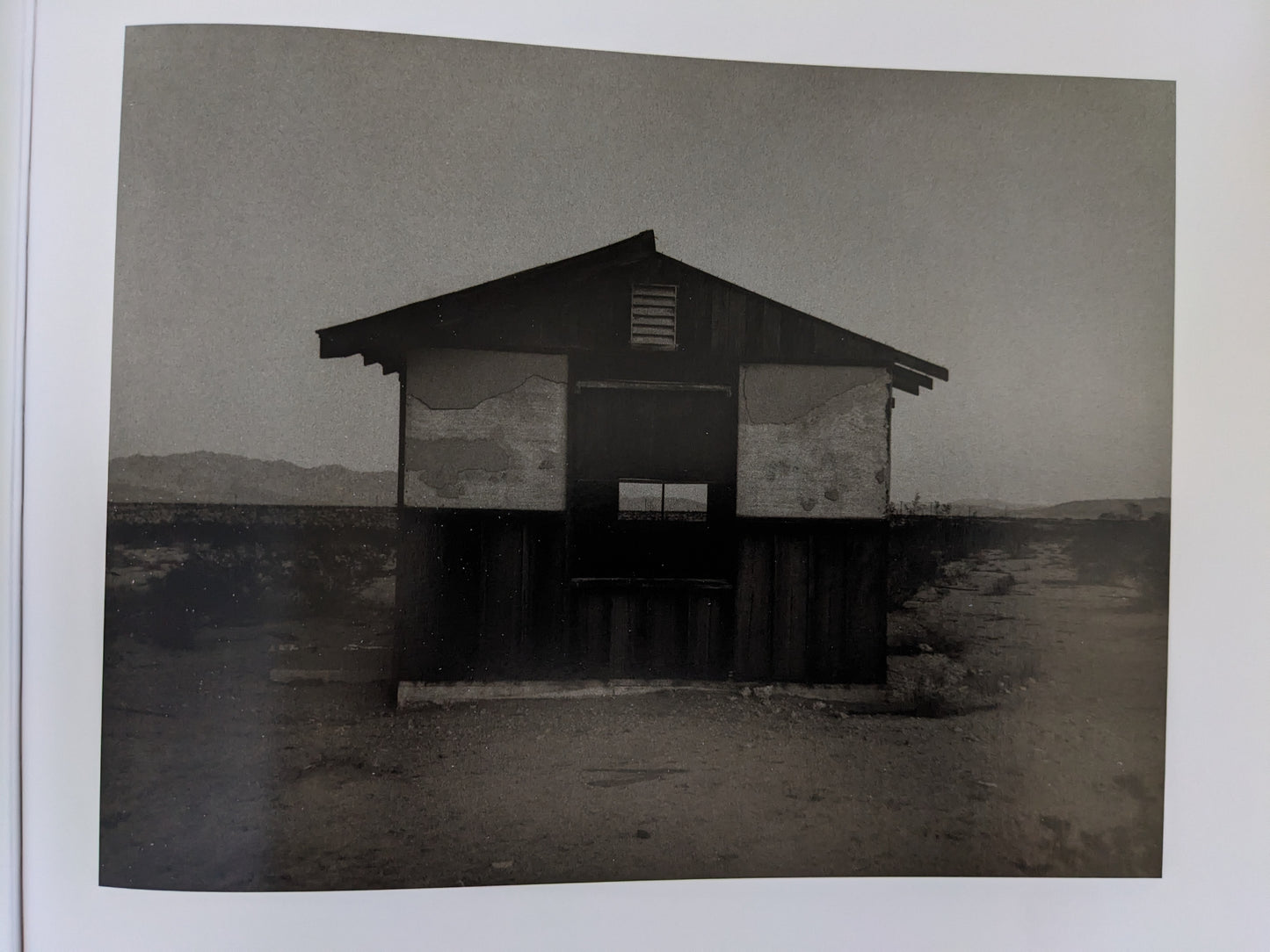 Front view of an abandoned single-room desert house with peeling paint and distant mountains