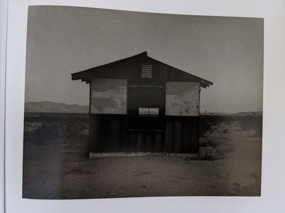 Front view of an abandoned single-room desert house with peeling paint and distant mountains