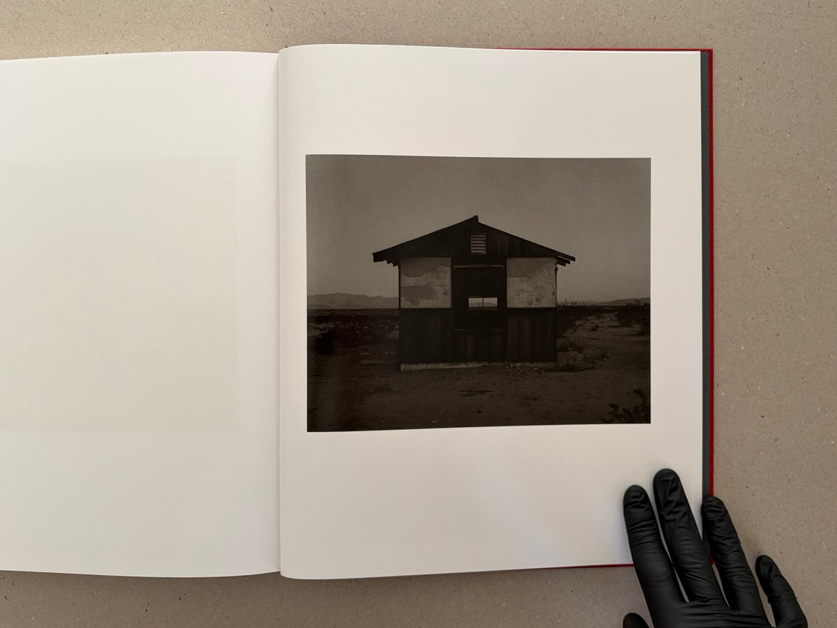 Open book showing a black-and-white photograph of a small desert house in Message from the Exterior by Mark Ruwedel.