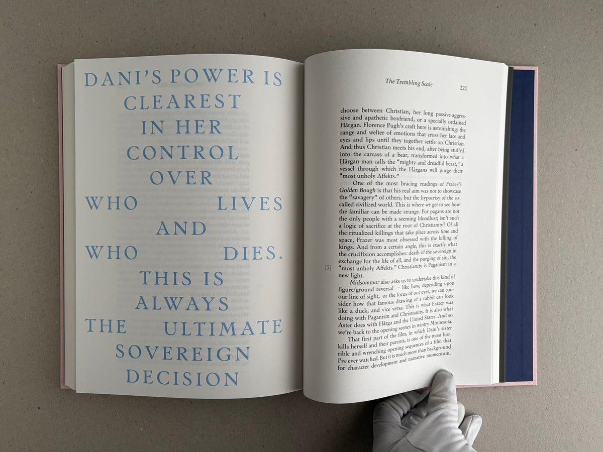 Open spread of Midsommar Screenplay Book, showing a blue typographic page on the left and a text page on the right, with a gloved hand holding the lower edge.