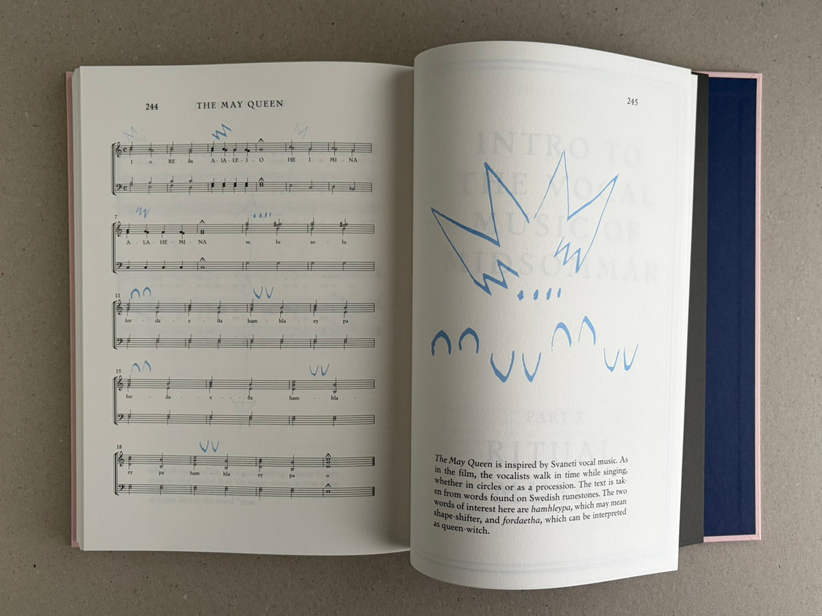 Open spread of the Midsommar Screenplay Book, showing printed music notation on the left page and a blue line drawing on the right page.