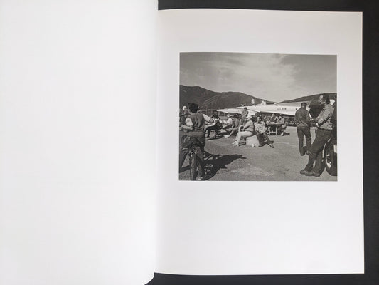 Interior spread from Mimi Plumb’s Landfall showing people gathered near an aircraft on an airfield.