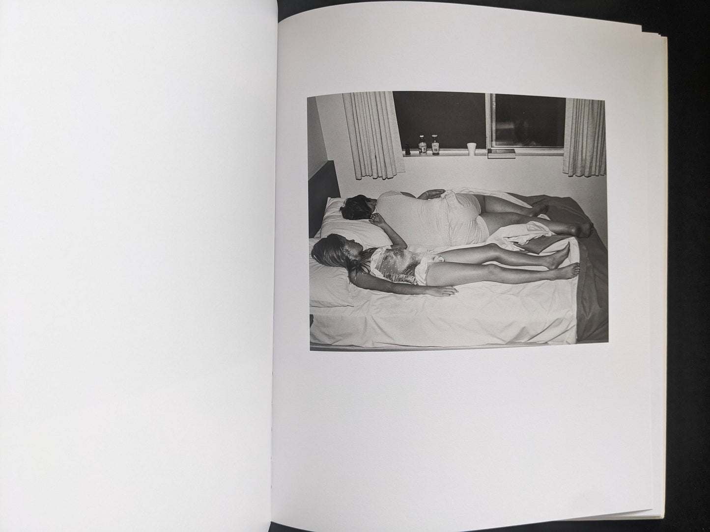 Interior photograph from Mimi Plumb’s Landfall showing two people lying on a bed in a dim room.