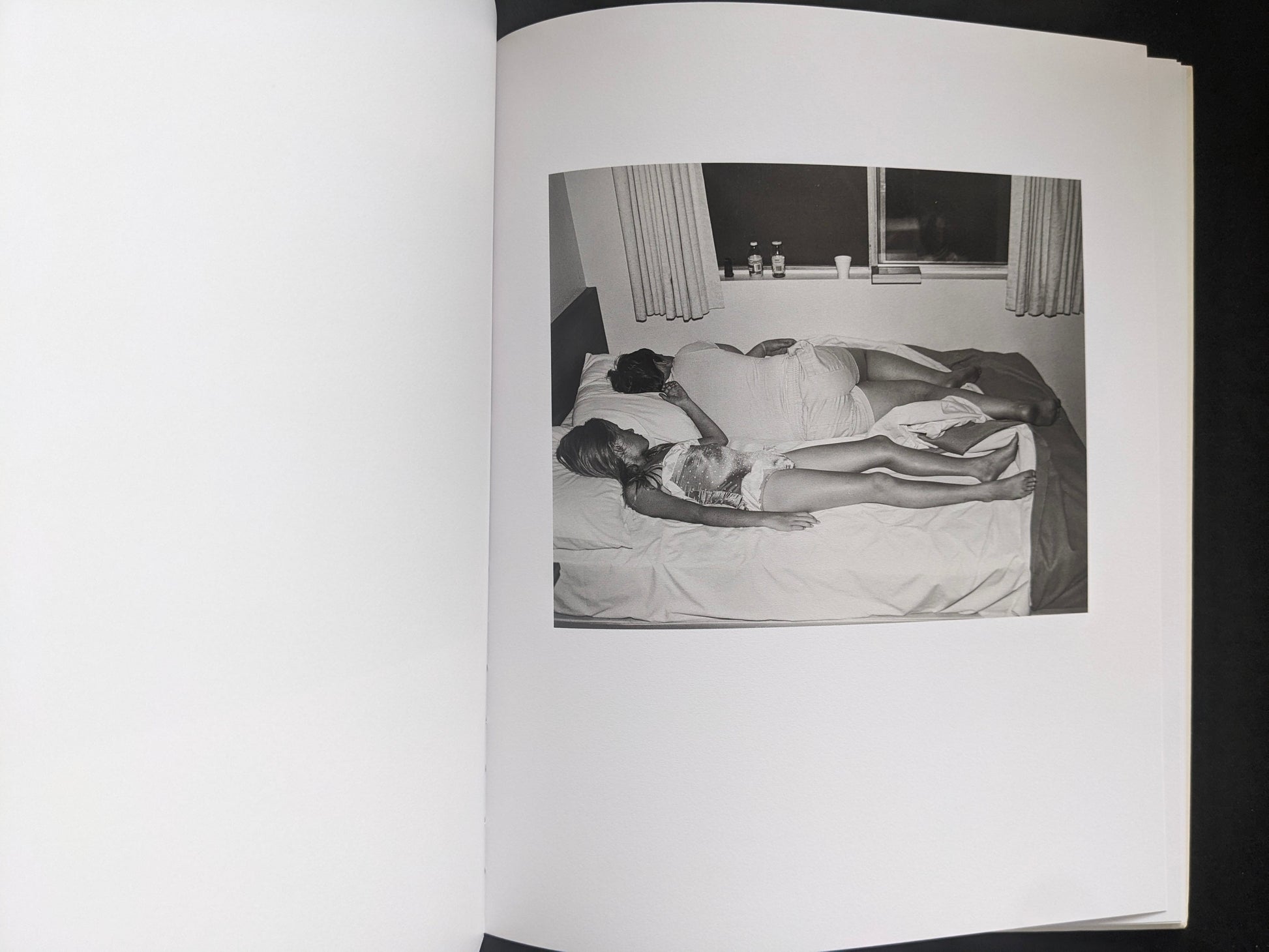 Interior photograph from Mimi Plumb’s Landfall showing two people lying on a bed in a dim room.