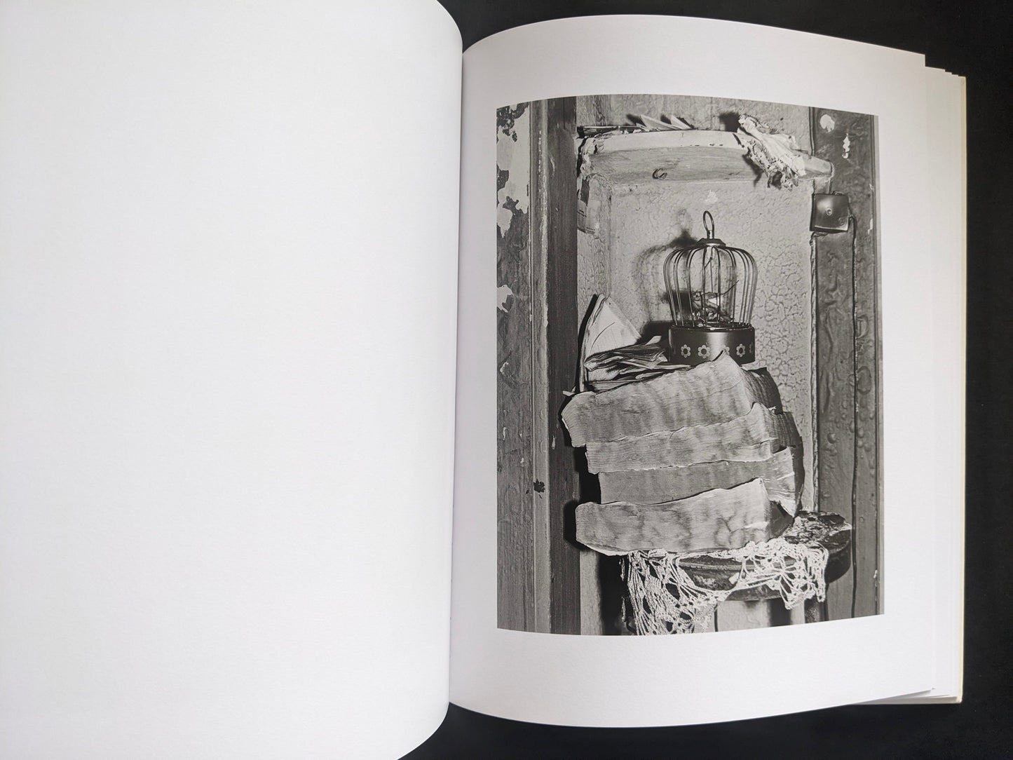 Interior photograph from Mimi Plumb’s Landfall showing a birdcage and stacked textiles in a worn interior.