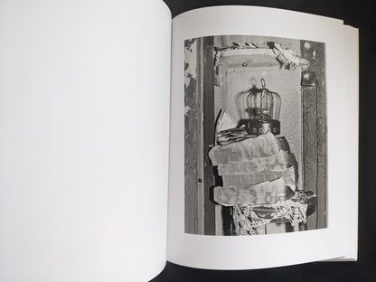 Interior photograph from Mimi Plumb’s Landfall showing a birdcage and stacked textiles in a worn interior.