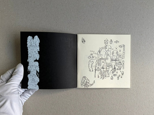 Open sketchbook spread from Multiforce Shit by Mat Brinkman, showing a black left page with a pale blue vertical drawing and a right page with a dense pen sketch of figures and symbols.