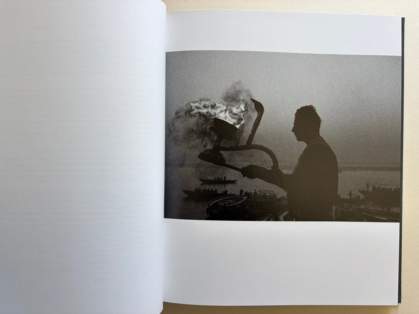 Interior photograph from Naked City Varanasi showing a silhouetted figure beside ritual fire and smoke at the riverfront.