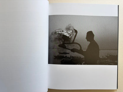 Interior photograph from Naked City Varanasi showing a silhouetted figure beside ritual fire and smoke at the riverfront.