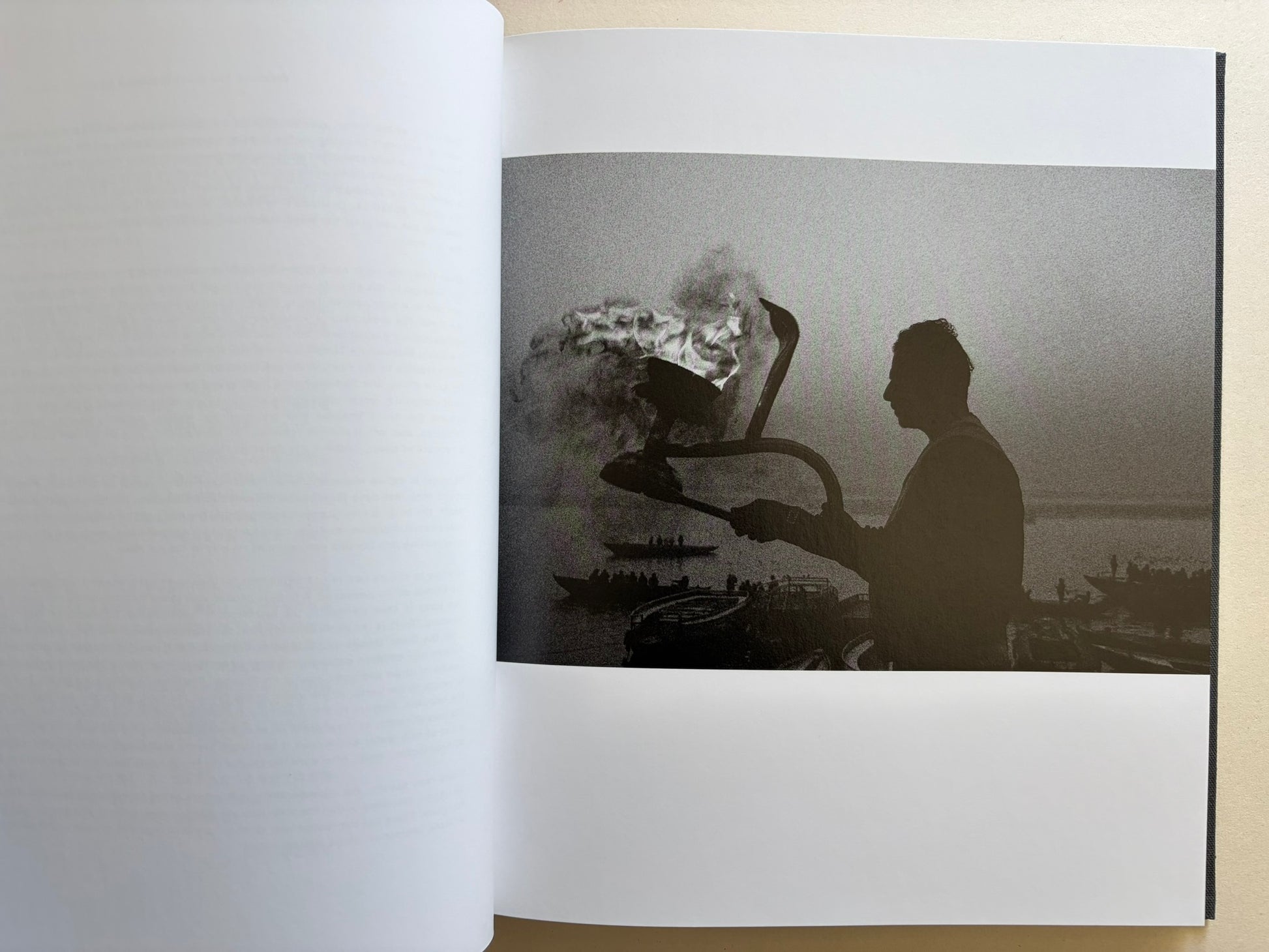 Interior photograph from Naked City Varanasi showing a silhouetted figure beside ritual fire and smoke at the riverfront.