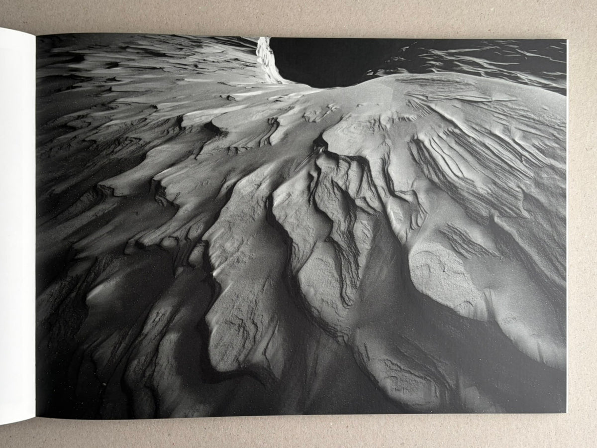 Open book spread showing a black-and-white landscape photograph from New Land: Pre-Hokkaido Landscapes by Toshiki Nakanishi, with textured snow or ice formations filling the page.