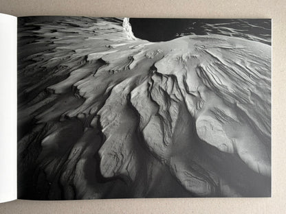 Open book spread showing a black-and-white landscape photograph from New Land: Pre-Hokkaido Landscapes by Toshiki Nakanishi, with textured snow or ice formations filling the page.