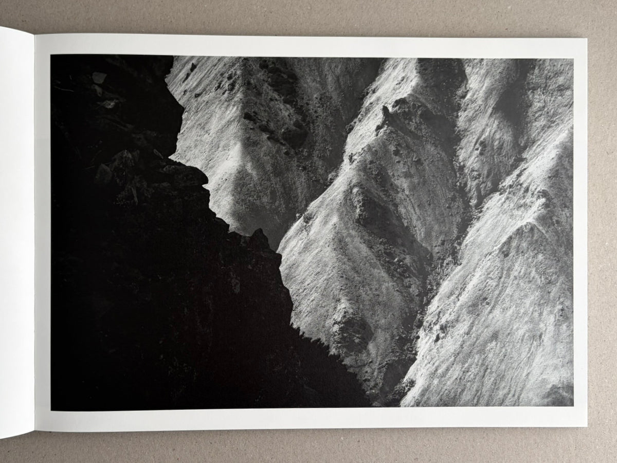Open photobook spread from New Land: Pre-Hokkaido Landscapes by Toshiki Nakanishi, showing a black-and-white landscape photograph of steep, snow-covered ridges.