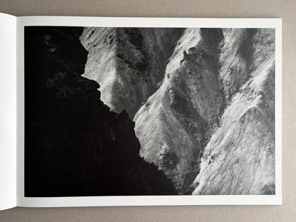 Open photobook spread from New Land: Pre-Hokkaido Landscapes by Toshiki Nakanishi, showing a black-and-white landscape photograph of steep, snow-covered ridges.