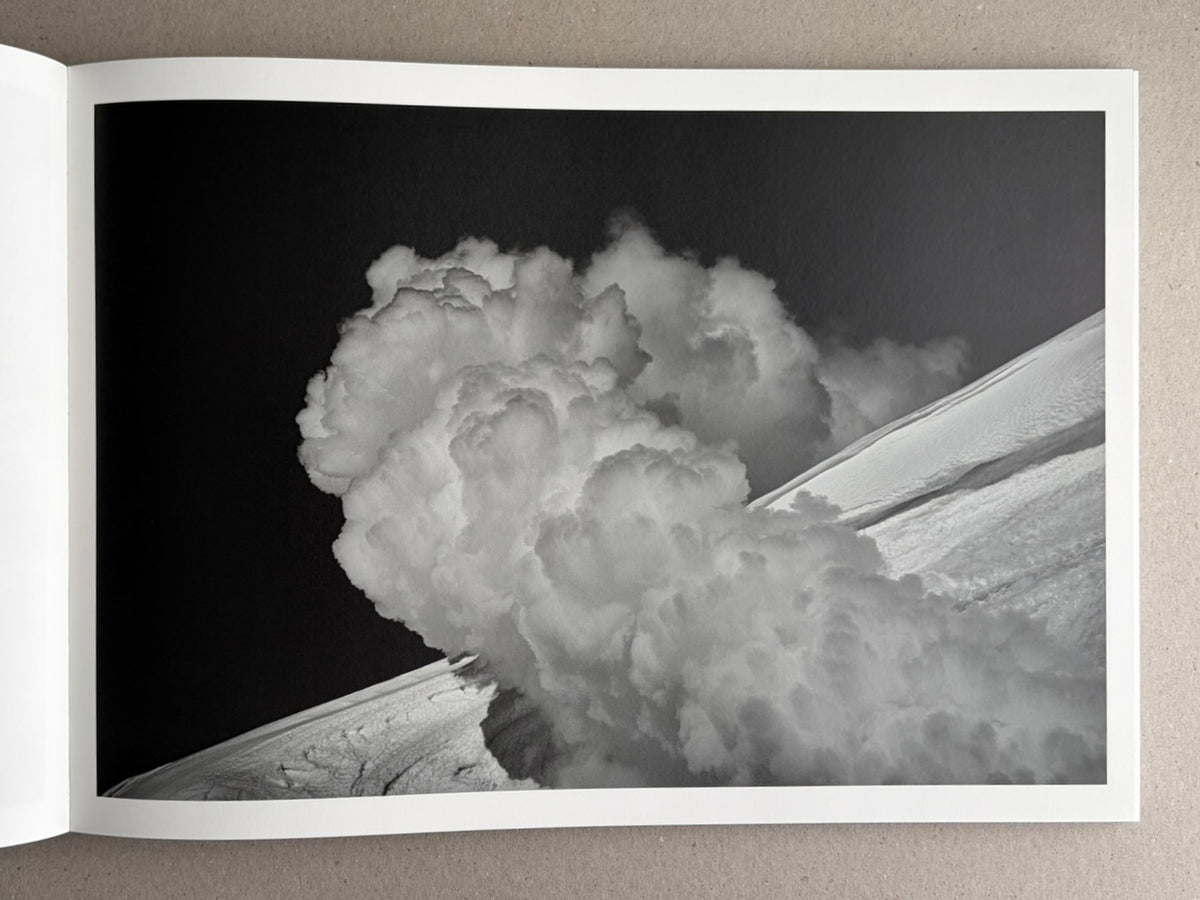 Open book spread showing a black-and-white photograph from New Land: Pre-Hokkaido Landscapes by Toshiki Nakanishi, with a large cloud-like plume over a sloping landscape.