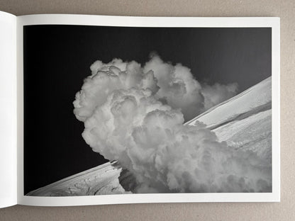 Open book spread showing a black-and-white photograph from New Land: Pre-Hokkaido Landscapes by Toshiki Nakanishi, with a large cloud-like plume over a sloping landscape.