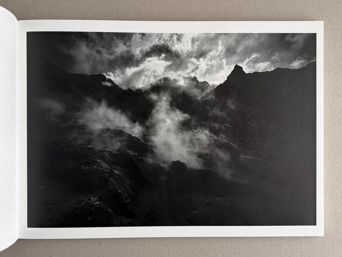 Open book spread showing a black-and-white mountain landscape with clouds and mist, from New Land: Pre-Hokkaido Landscapes by Toshiki Nakanishi.