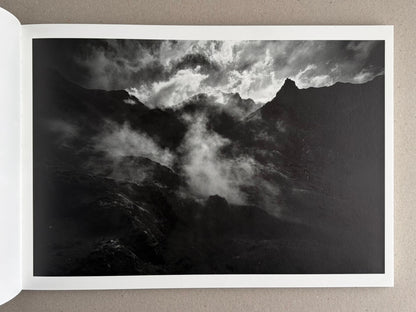 Open book spread showing a black-and-white mountain landscape with clouds and mist, from New Land: Pre-Hokkaido Landscapes by Toshiki Nakanishi.