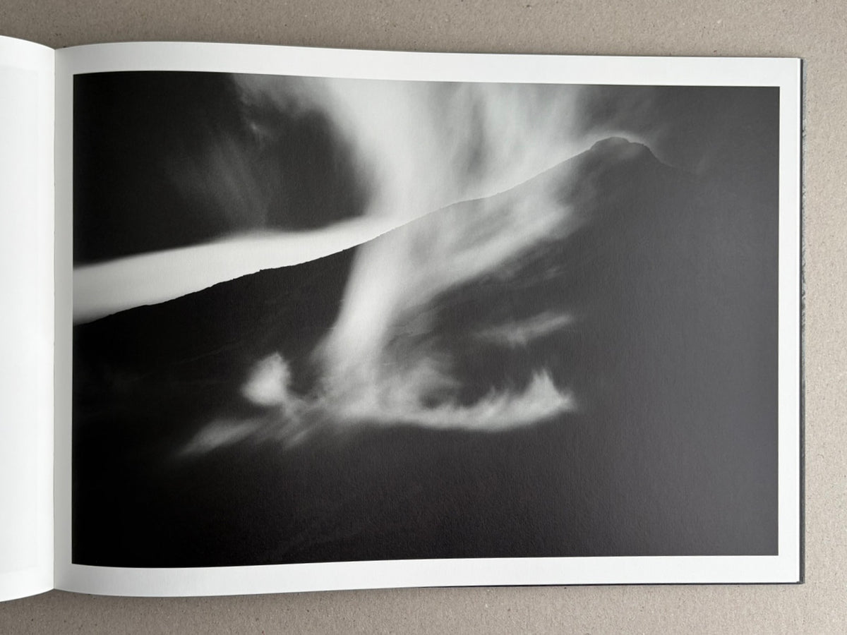 Open photobook spread showing a black-and-white landscape image with a dark mountain silhouette and blurred light streaks across the page.
