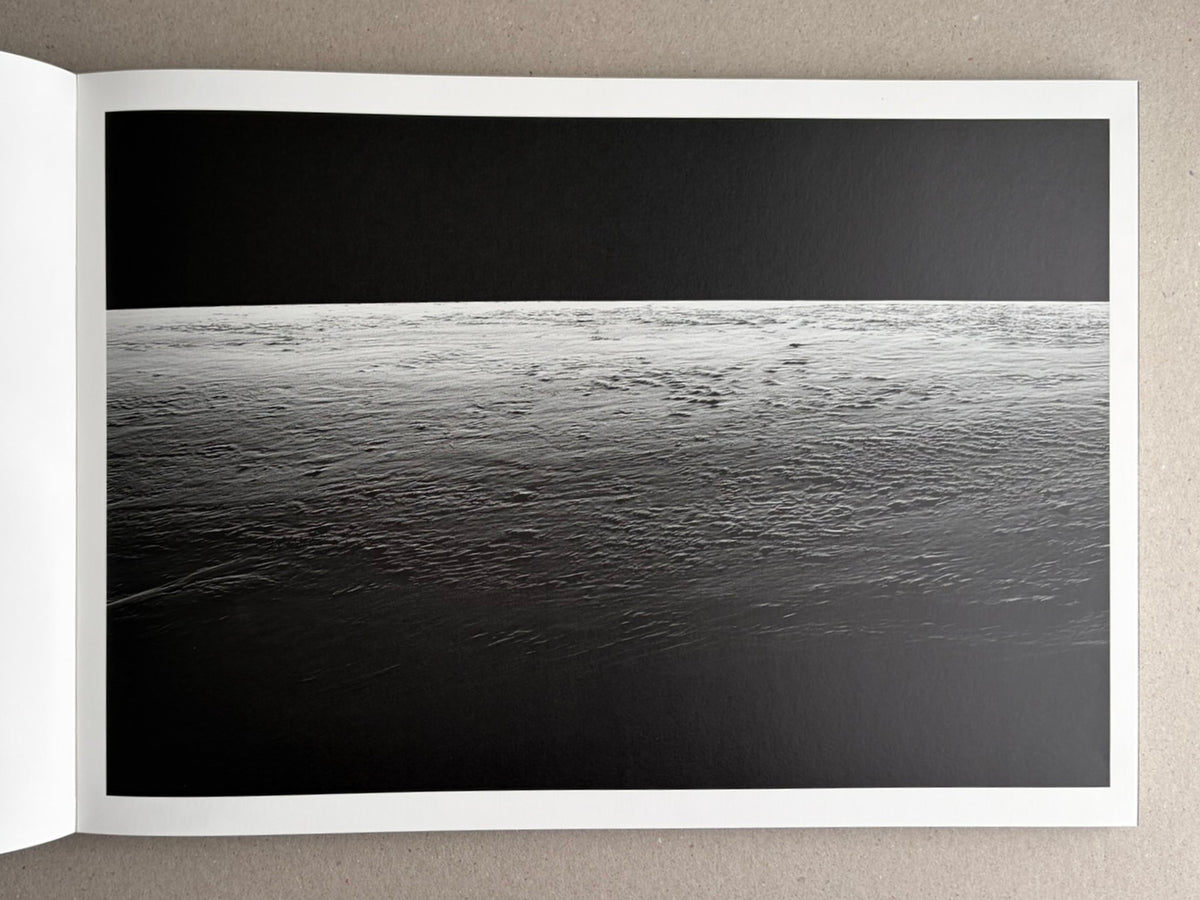 Open photobook spread from New Land: Pre-Hokkaido Landscapes by Toshiki Nakanishi, showing a black-and-white seascape across the page.
