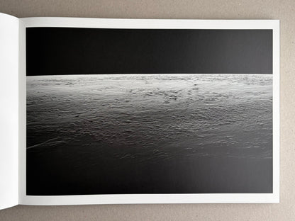Open photobook spread from New Land: Pre-Hokkaido Landscapes by Toshiki Nakanishi, showing a black-and-white seascape across the page.