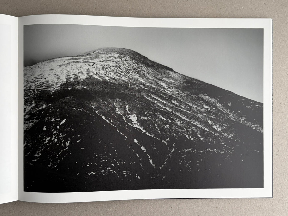 Open photobook spread showing a black-and-white landscape photograph of a snow-covered mountain slope.