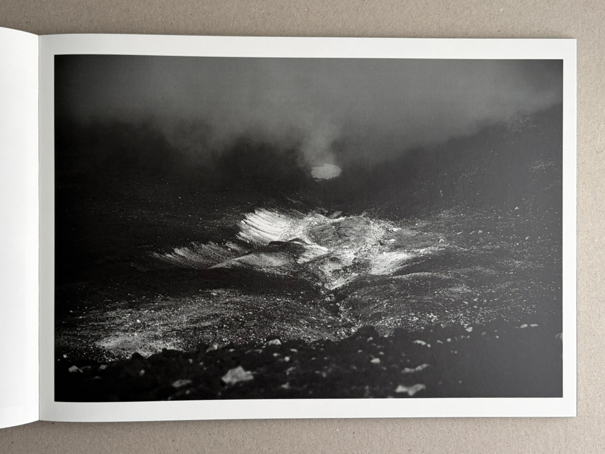 Open photobook page showing a black-and-white landscape photograph of a dark, misty rocky scene.