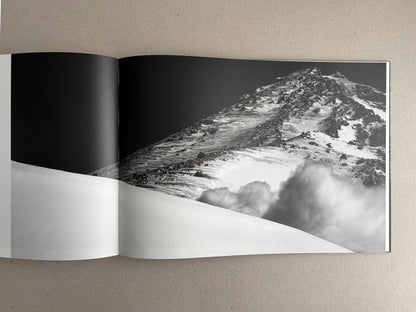 Open photobook spread from New Land: Pre-Hokkaido Landscapes by Toshiki Nakanishi, showing a black-and-white mountain landscape with snow and cloud forms.