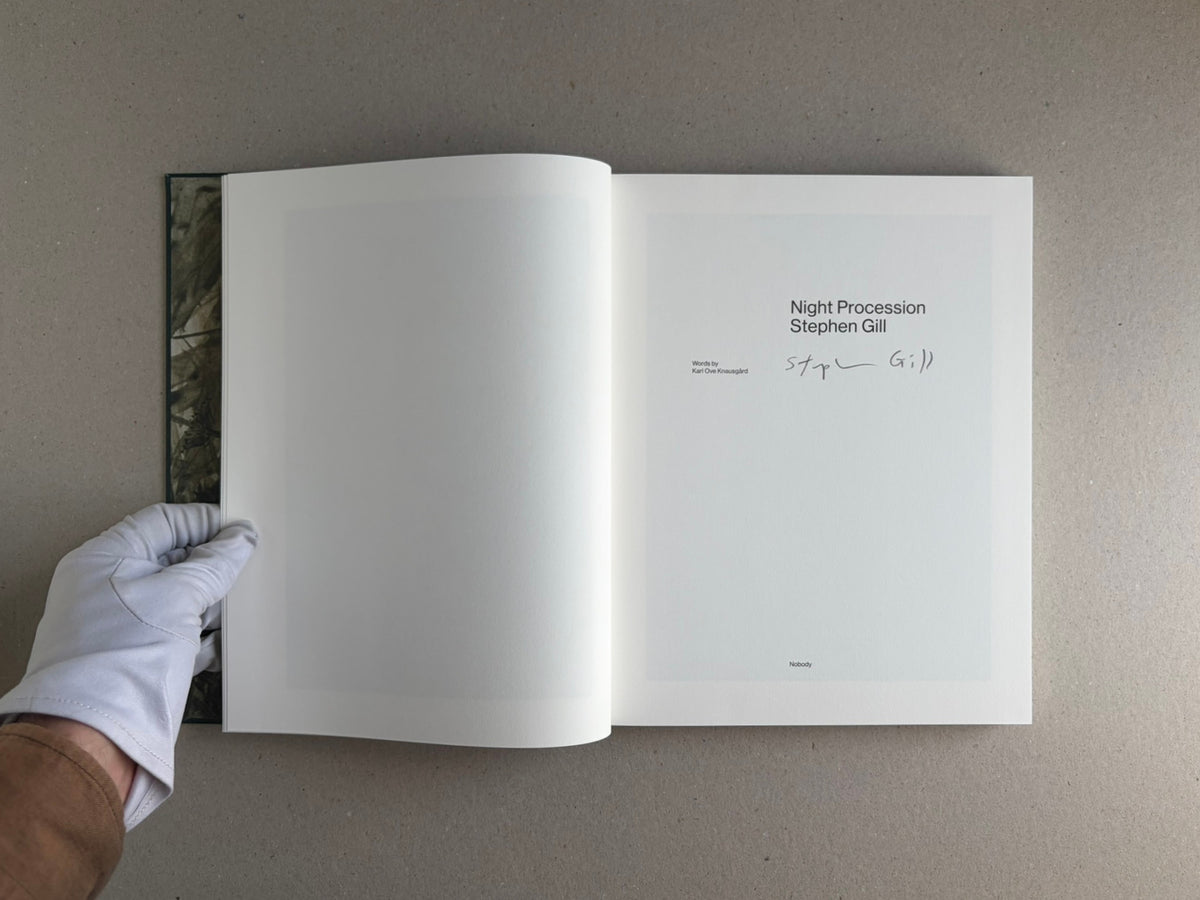 Open signed copy of Night Procession by Stephen Gill, showing the title page with his signature and a gloved hand holding the book