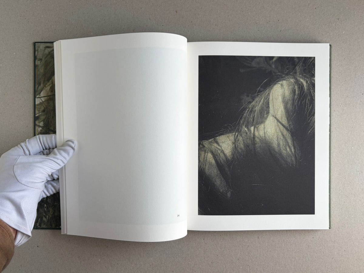 Open copy of Night Procession by Stephen Gill, showing a blank left page and a black-and-white image on the right page, with a gloved hand holding the book open.