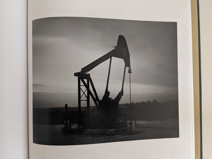 Black-and-white photograph of an oil pumpjack in the American West from No Fences by Mark McLennan