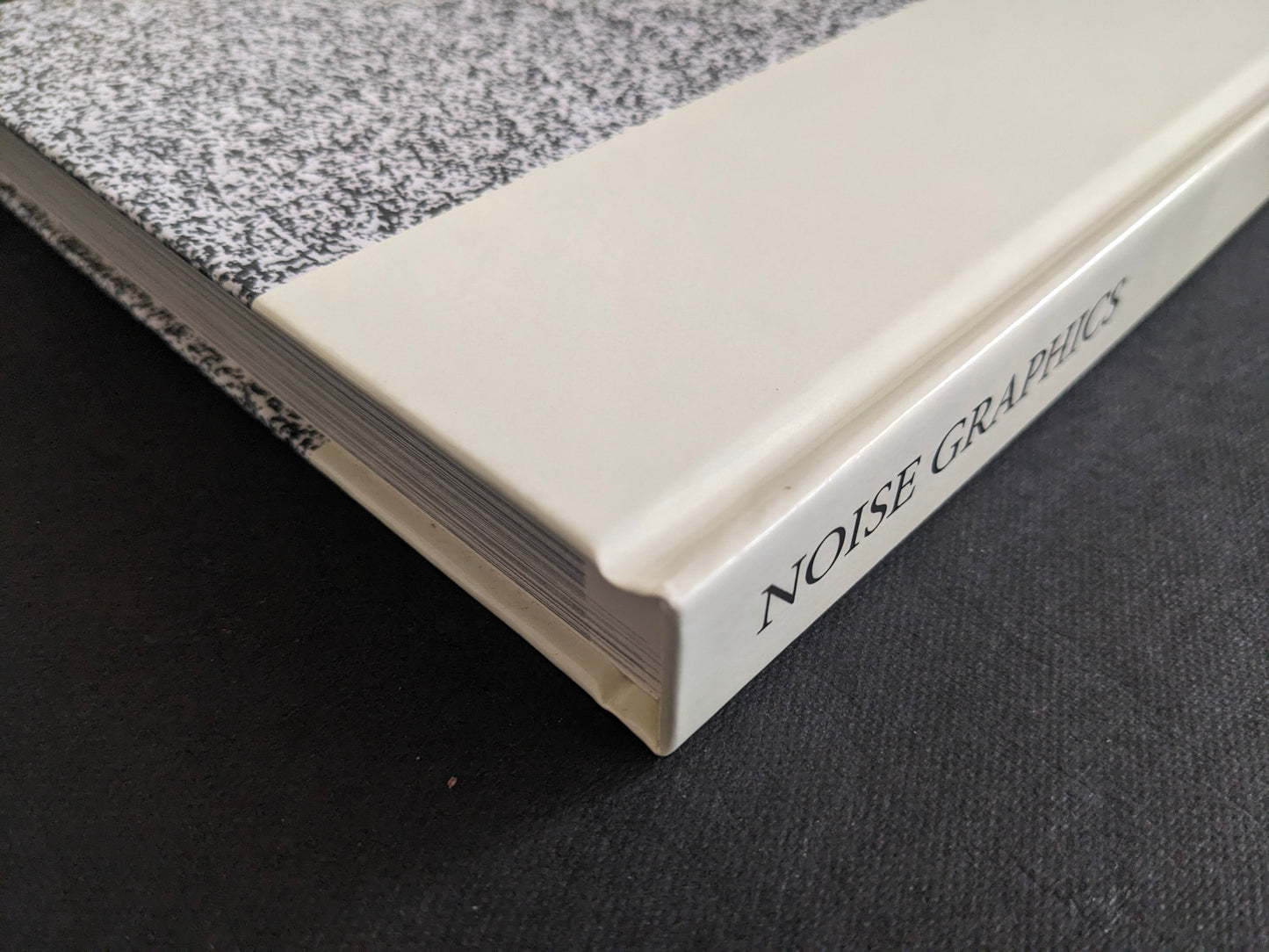 Noise Graphics 1980–1990 book spine detail with NOISE GRAPHICS title on a cream strip and a static-like black-and-white pattern.